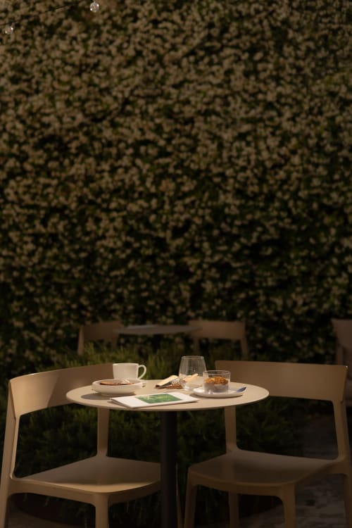Intimate outdoor dining setup at Hotel Fragile in Menorca with cream chairs, round table, and lush green hedge backdrop