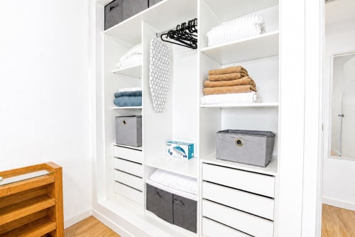 Armario blanco organizado con estantes, cajones, toallas, cajas de almacenamiento y perchas, apartamento en Valencia
