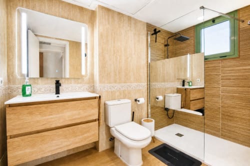 Baño moderno con paredes de madera, espejo iluminado, inodoro blanco y ducha de cristal en Pataconablue Rentals
