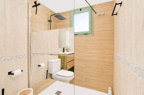 Baño moderno con azulejos con veta de madera, ducha de cristal, inodoro blanco y espejo con marco verde en apartamento frente al mar en Valencia