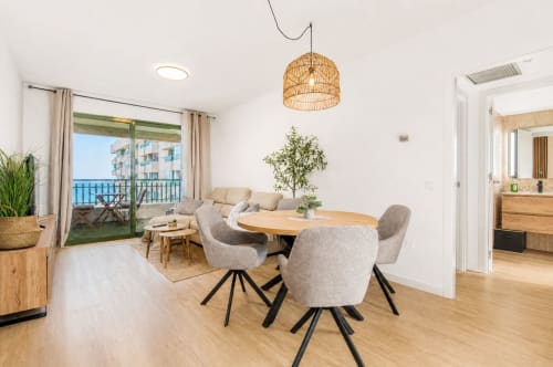 Comedor moderno con vista al mar, balcón, mesa de madera, sillas grises y lámpara colgante tejida en Valencia