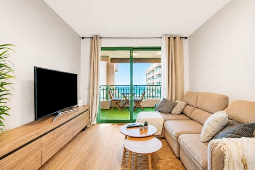 Salón luminoso de apartamento frente al mar en Valencia con balcón con vistas, sofá, TV y decoración moderna