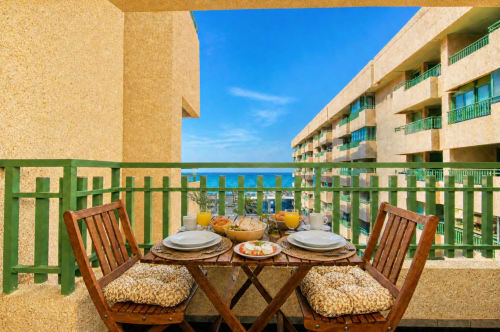 Balcón de apartamento frente al mar en Valencia con mesa de comedor, sillas de madera, vista al mar y barandilla verde