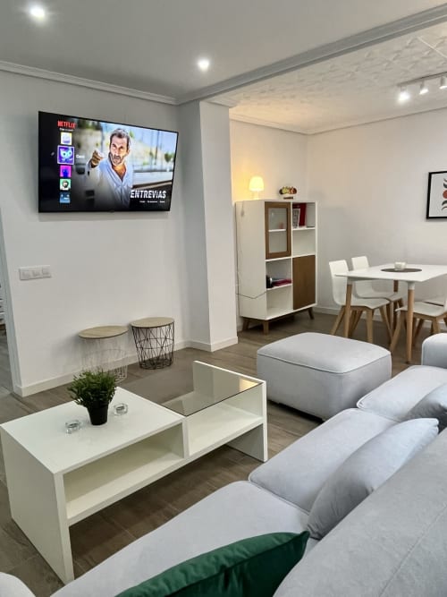 Sala de estar moderna de apartamento en Valencia con sofá, TV Netflix, mesa de comedor y unidad de almacenamiento