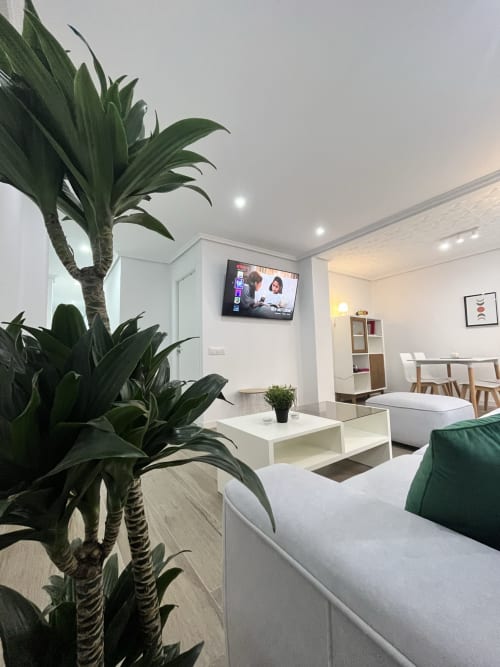 Moderno salón de apartamento en Valencia con plantas verdes, sofá blanco, televisor y área de comedor en Pataconablue Rentals