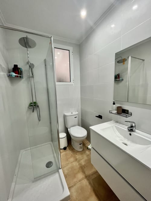 Cuarto de baño moderno en apartamento de Valencia con ducha, inodoro y lavamanos blanco con espejo