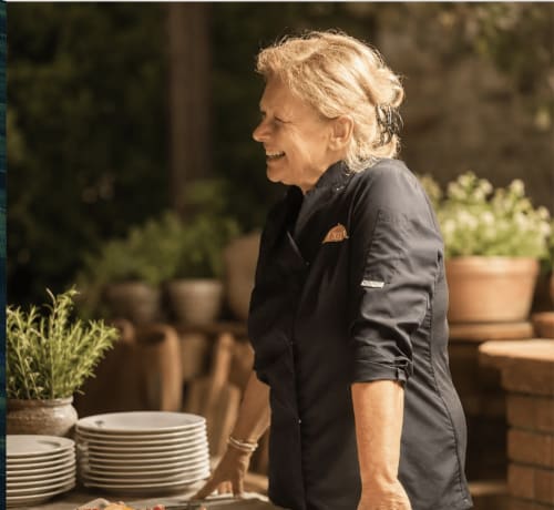 Direttore di Casa Pineta sorridente nel cortile elegante con piante in vaso e piatti impilati a Marina di Campo
