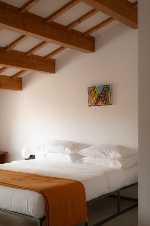 Modern hotel bedroom at Hotel Fragile in Menorca with exposed wooden beams, white bedding, colorful artwork, and minimalist