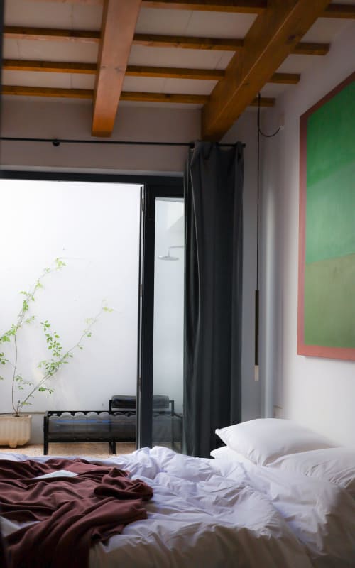 Modern bedroom at Hotel Fragile in Menorca with wooden beams, black canopy bed, and colorful accent walls