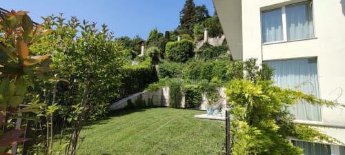Grüner Garten mit Rasen im Prince Garda Hotel in Salò, umgeben von efeubedeckten Mauern und modernem Gebäude