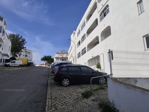 Carro preto estacionado no complexo de apartamentos Albufeira Inn no centro da cidade com edifício residencial branco e céu azul limpo