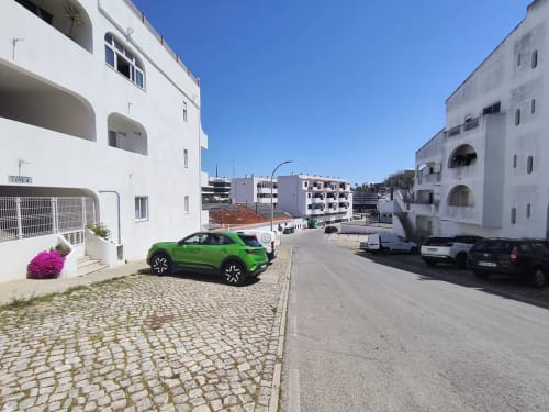 Carro verde estacionado na Albufeira Inn, edifício com arquitetura branca e flores cor-de-rosa, centro de Albufeira