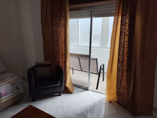Varanda CASA FLOR no Albufeira Inn com cortinas com padrão marrom, poltrona preta e vista da cidade