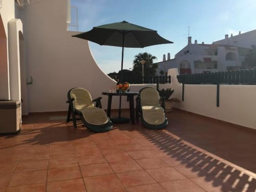 Terraço ensolarado no Albufeira Inn com duas espreguiçadeiras, guarda-sol preto e mesa com vista para os jardins do Mediterrâneo