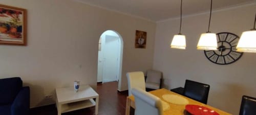 Luminosa sala de estar do apartamento Albufeira Inn com área de refeições, sofá, luminárias pendentes e entrada em arco para quarto