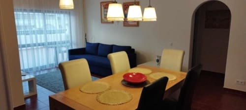 Sala de jantar moderna com mesa de madeira, cadeiras amarelas e sofá azul no apartamento Albufeira Inn, Portugal