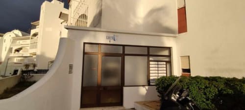 Entrada do apartamento térreo da Albufeira Inn com fachada branca, portas de madeira e plantas verdes exuberantes em Praia dos Aveiros