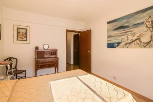 Quarto luminoso no apartamento Albufeira Inn com cama de madeira, cômoda antiga, quadros emoldurados e vista para a cidade da varanda