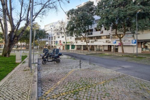 Centro histórico de Albufeira com edifícios antigos, praça de paralelepípedos, scooter junto às árvores, frente do Albufeira Inn
