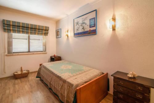 Quarto aconchegante no apartamento Albufeira Inn com cama de madeira, cômoda, janela com cortina xadrez e arte náutica na parede