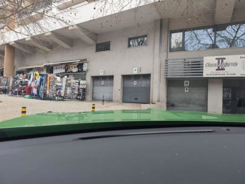 Fachada do edifício de apartamentos Albufeira no centro da cidade com capô de carro verde em primeiro plano, vitrines comerciais visíveis