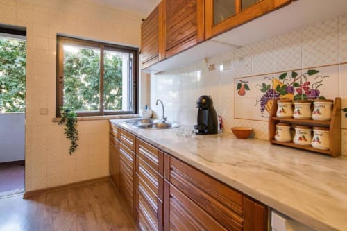 Cozinha clara com armários em madeira, bancada em mármore e vista pela janela no apartamento Albufeira Inn em Portugal