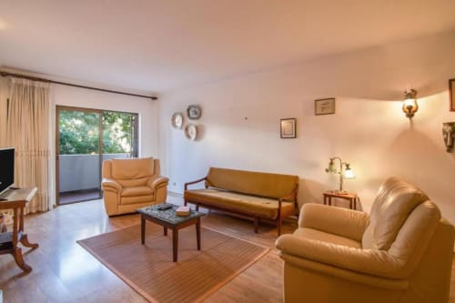Ampla sala de estar do apartamento Albufeira Inn com assentos de couro bege, sofá-cama, mesa de café em madeira e vista da cidade