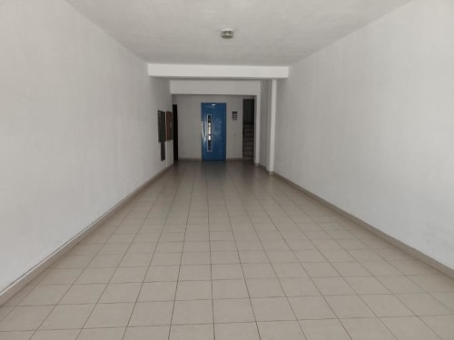 Corredor vazio do apartamento Albufeira Inn com pisos em azulejo, paredes brancas, porta azul e acesso ao elevador