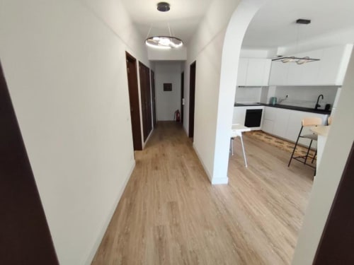 Corredor moderno do apartamento Albufeira Inn com cozinha, piso de madeira e portas para os quartos