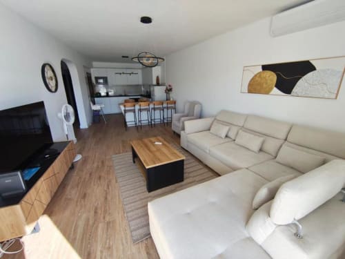 Sala de estar moderna em Albufeira com sofá creme, móveis de madeira, kitchenette e decoração costeira perto da Praia dos