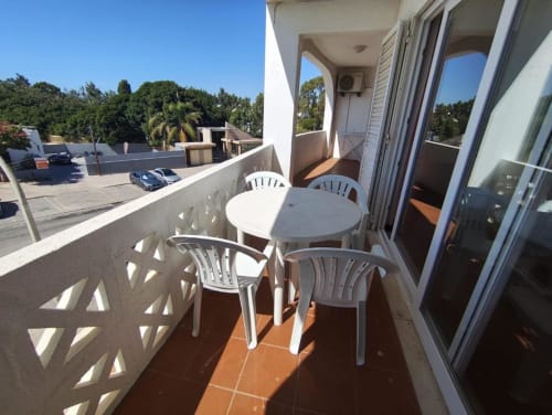Terraço ensolarado da Albufeira Inn com mesa e cadeiras brancas, vista para estacionamento e árvores em Praia dos Aveiros