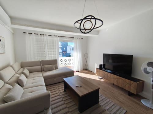 Sala moderna em apartamento de Albufeira com sofá bege, TV, mesa de madeira e varanda com vista