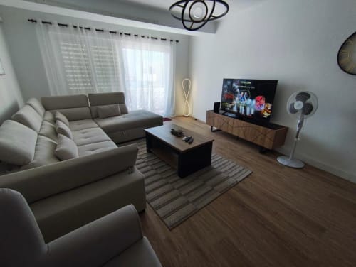 Sala de estar moderna em apartamento de praia em Albufeira com sofá cinzento, TV, piso em madeira e móveis contemporâneos