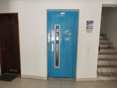 Elevador azul no edifício Albufeira Inn com paredes brancas e piso em azulejo, acessível para pisos superiores