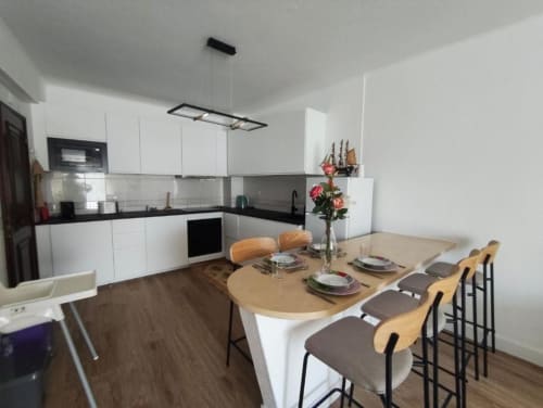 Cozinha moderna branca e área de refeições em apartamento em Albufeira, a 5 minutos da praia, com mesa em madeira e assentos no bar
