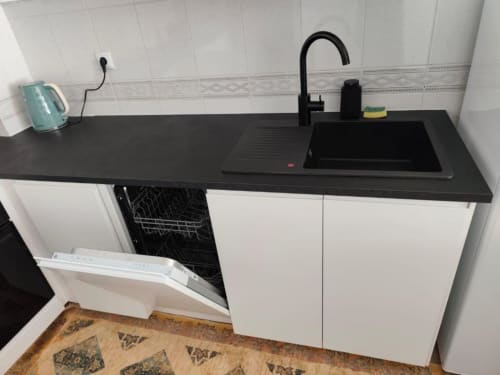 Cozinha moderna com bancada preta, armários brancos, pia preta, máquina de lavar louça e fogão em apartamento à beira-mar em Albufeira