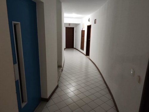 Corredor limpo do apartamento Albufeira Inn com parede de destaque azul, piso em azulejos, portas de madeira escura e iluminação brilhante
