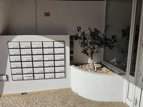 Entrada do apartamento Albufeira Inn com caixas de correio e vaso de plantas no alpendre branco, Praia dos Aveiros