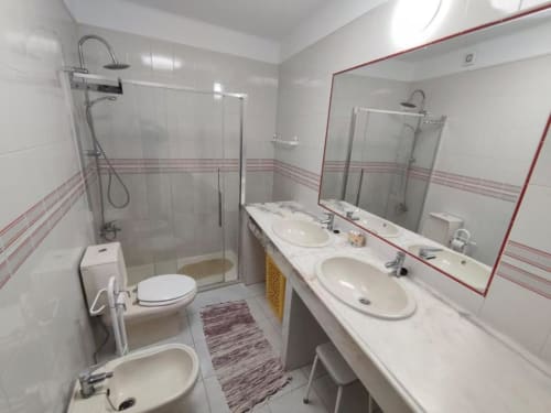 Banheiro moderno com dois lavatórios, box de chuveiro e vaso sanitário no apartamento Albufeira Inn perto da Praia dos Aveiros