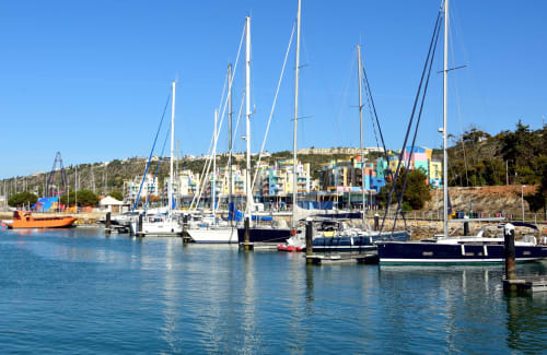 Barcos à vela atracados na marina de Albufeira com edifícios coloridos à beira-mar e céu azul cristalino
