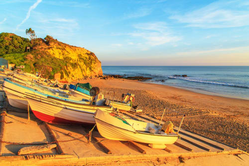 Barcos de pesca coloridos em praia de areia dourada em Albufeira, Portugal, com falésias costeiras e mar calmo ao pôr do sol