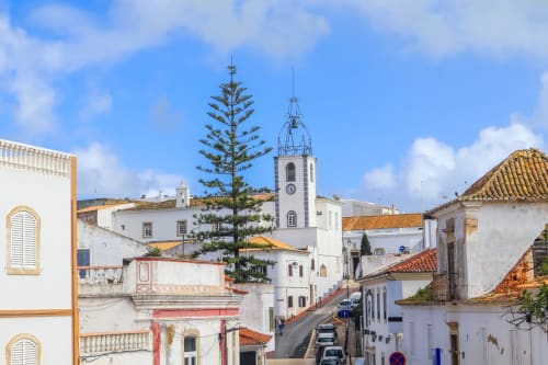Rua encantadora de Albufeira com edifícios brancos, torre do relógio da igreja e arquitetura portuguesa tradicional do Albufeira Inn