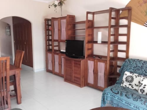 Sala de estar do apartamento Albufeira Inn com prateleiras de madeira, TV de tela plana, sofá e sala de jantar