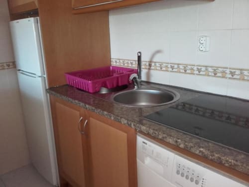 Cozinha moderna do apartamento Albufeira Inn com pia em aço inoxidável, fogão elétrico, refrigerador e bancada em granito