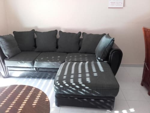 Sofá de canto cinzento moderno com almofadas decorativas em cores vibrantes em sala de estar de apartamento em Albufeira, com piso em azulejo e luz natural