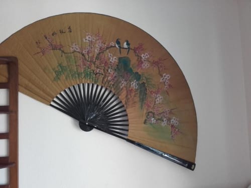 Leque chinês tradicional com galhos floridos rosa e pássaros pousados exibido na parede branca do apartamento Albufeira Inn.