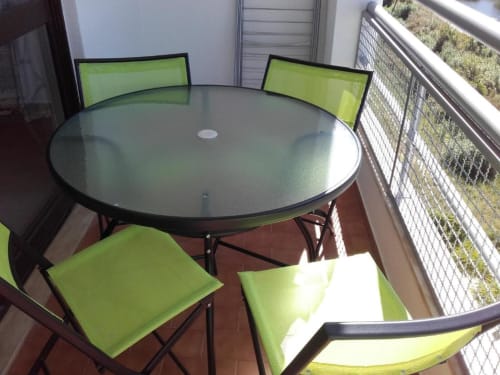 Zona de estar moderna na varanda com mesa redonda de vidro e cadeiras verde-lima no apartamento Albufeira Inn, com vista para o oceano