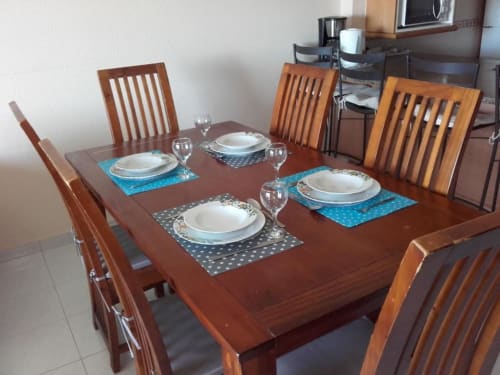 Mesa de jantar em madeira posta para quatro pessoas no apartamento Albufeira Inn, com prataria, copos e toalhas de mesa azuis