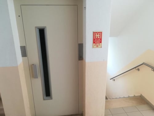 Escada do edifício de apartamentos Albufeira Inn com elevador e placa de emergência vermelha na parede