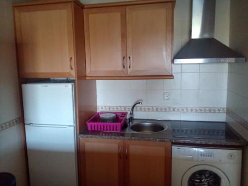 Kitchenette compacta no apartamento de Albufeira com armários em madeira, refrigerador Bosch, fogão, pia e máquina de lavar.